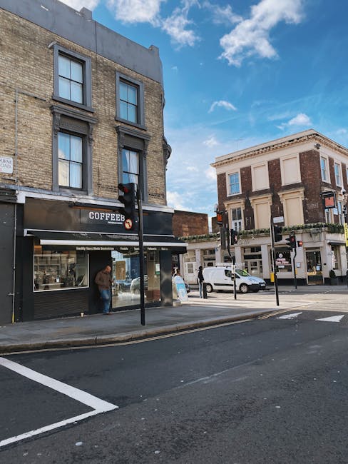 The exterior of a small shop with a prominent green and white sign reading 'GREEN SHOP' situated on Northcote Road in Clapham, featuring a large glass window and door displaying various posters and pr